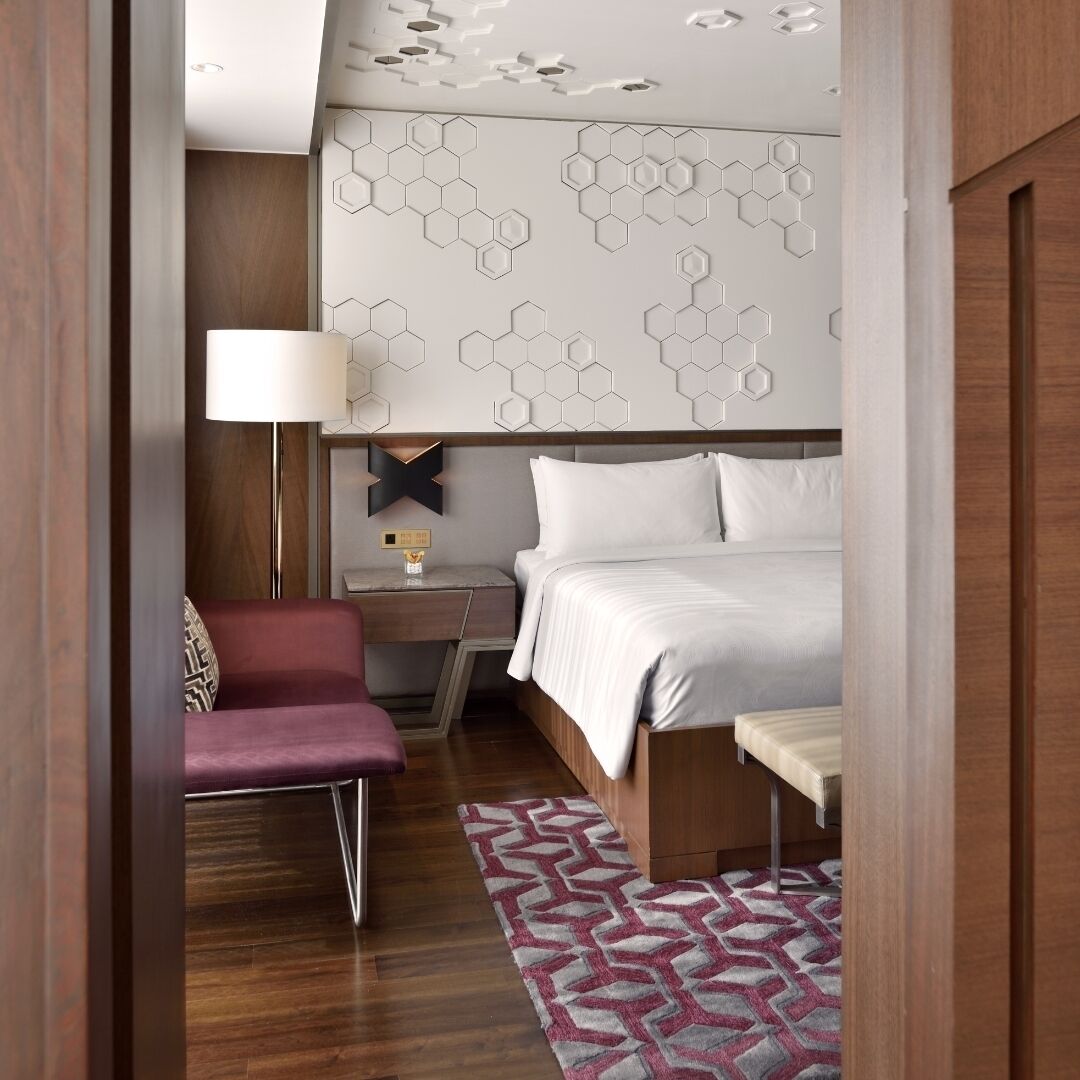 Une chambre d’hôtel moderne avec un lit, une table de chevet, une lampe et un tapis à motifs.