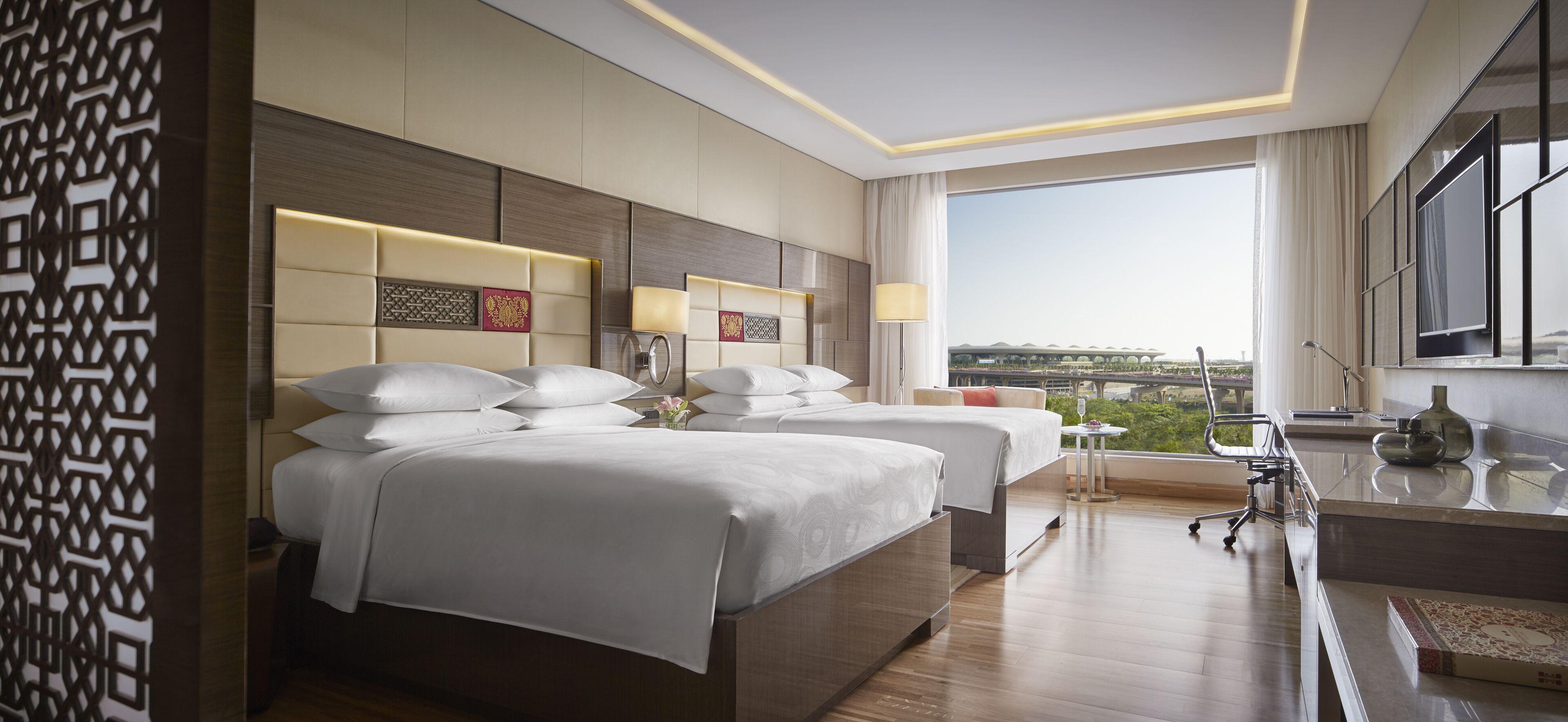 Habitación de hotel con dos camas, un escritorio, una silla y un ventanal con vistas a la ciudad.