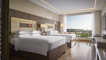 Habitación de hotel con dos camas, un escritorio, una silla y un ventanal con vistas a la ciudad.