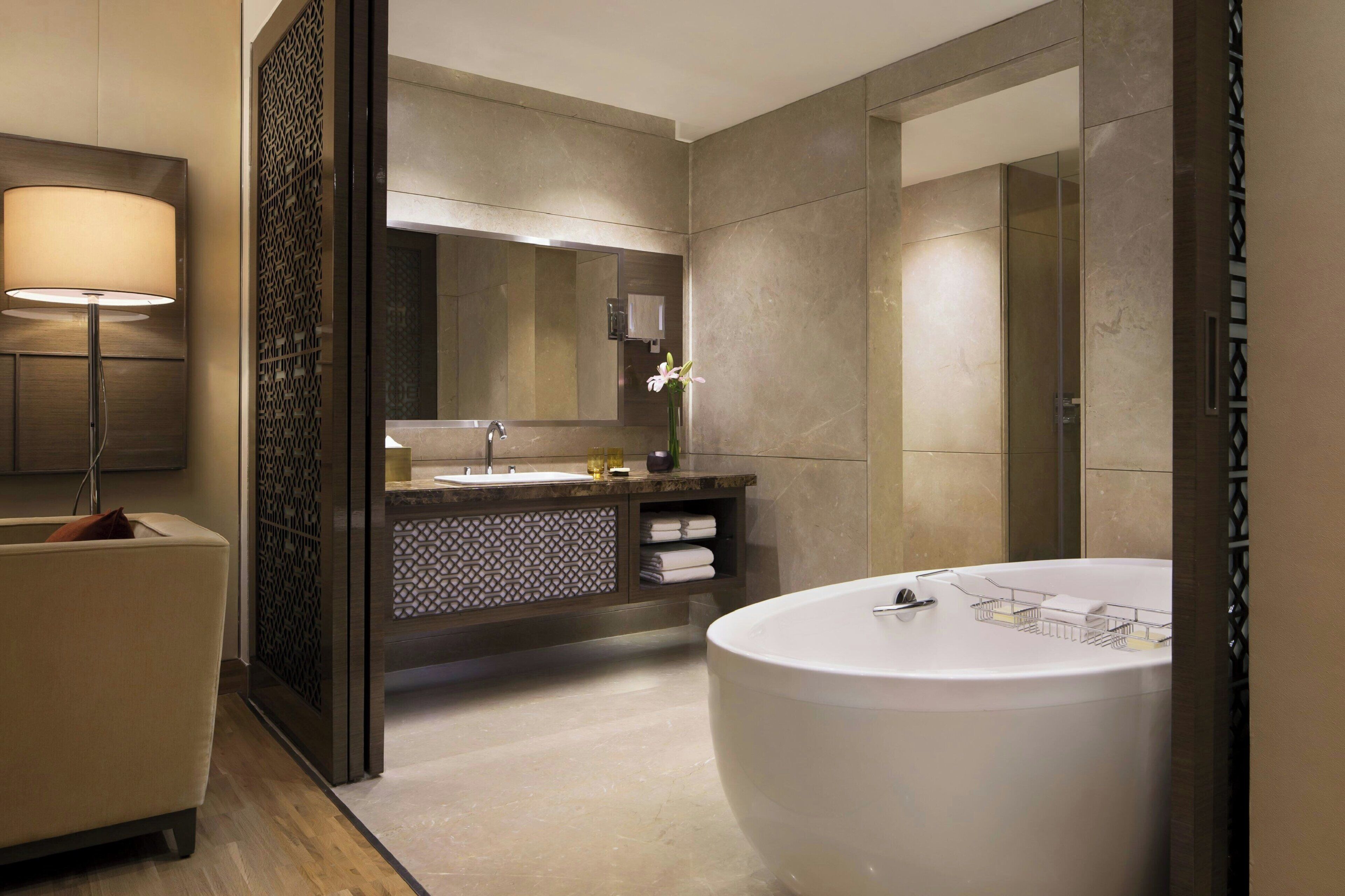 A modern bathroom with a large bathtub, a vanity with a mirror, and a floor lamp.