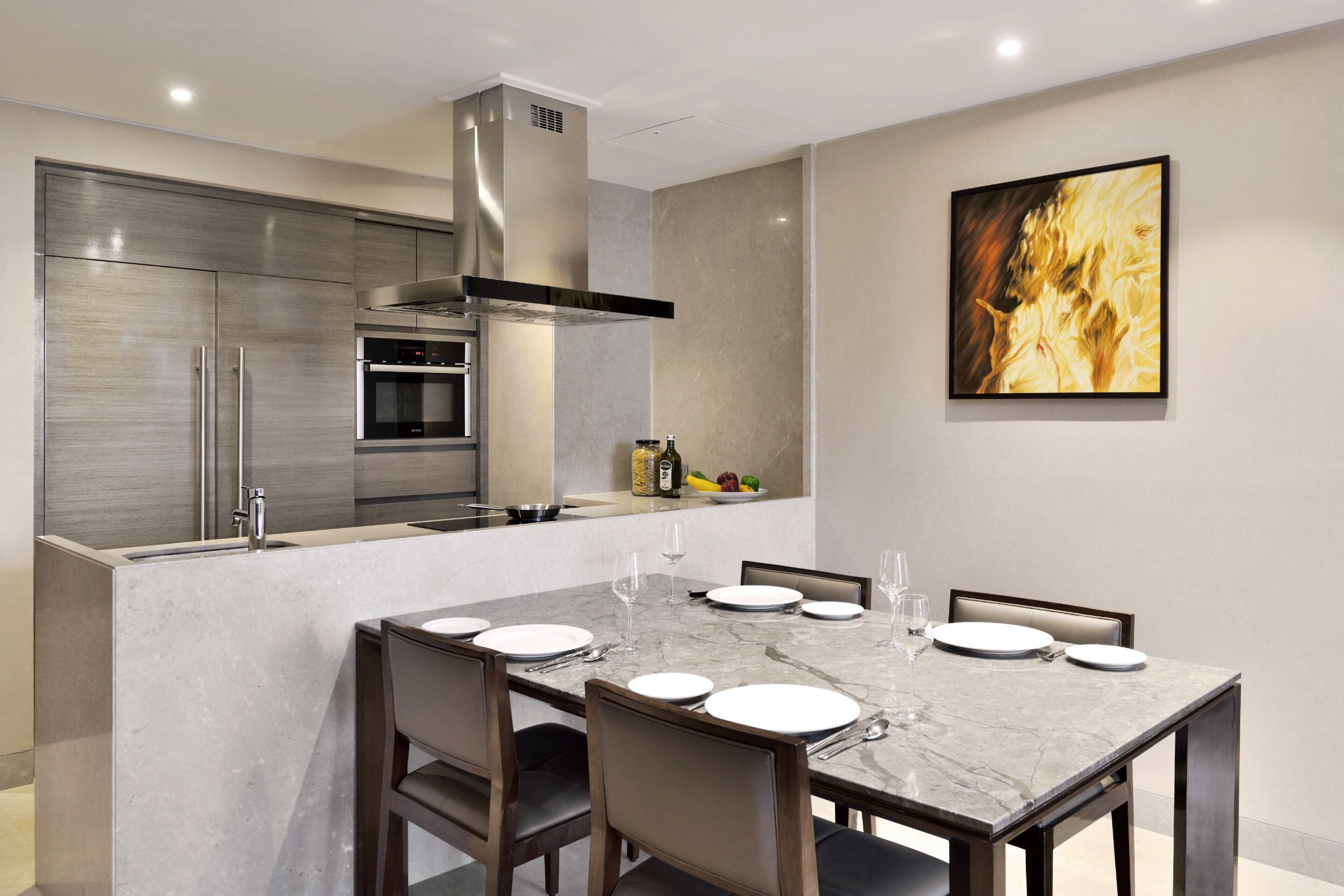 A modern kitchen with stainless steel appliances, a marble dining table, and a large painting on the wall.