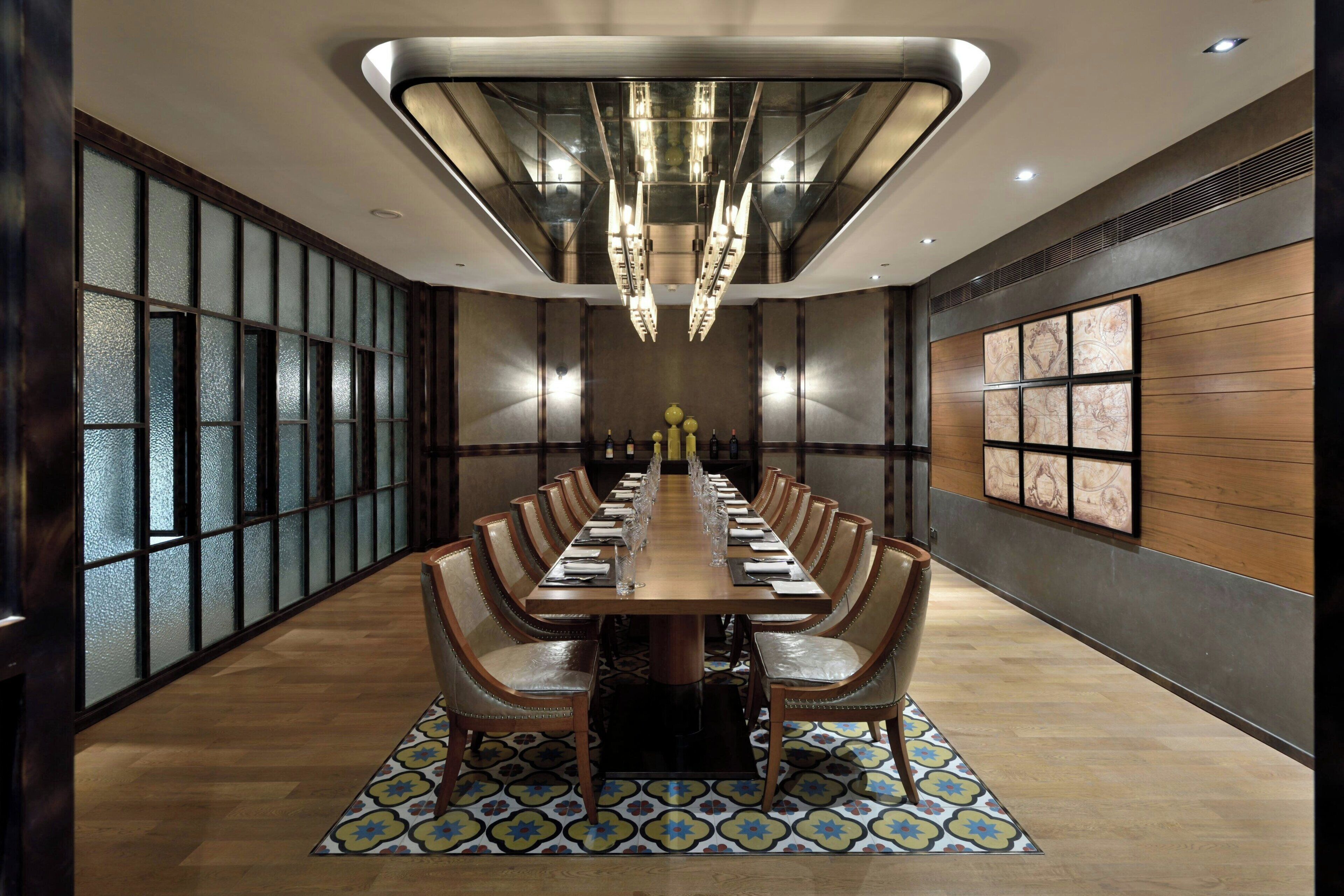Una larga mesa de comedor con sillas, un tapete estampado y una lámpara de araña moderna.