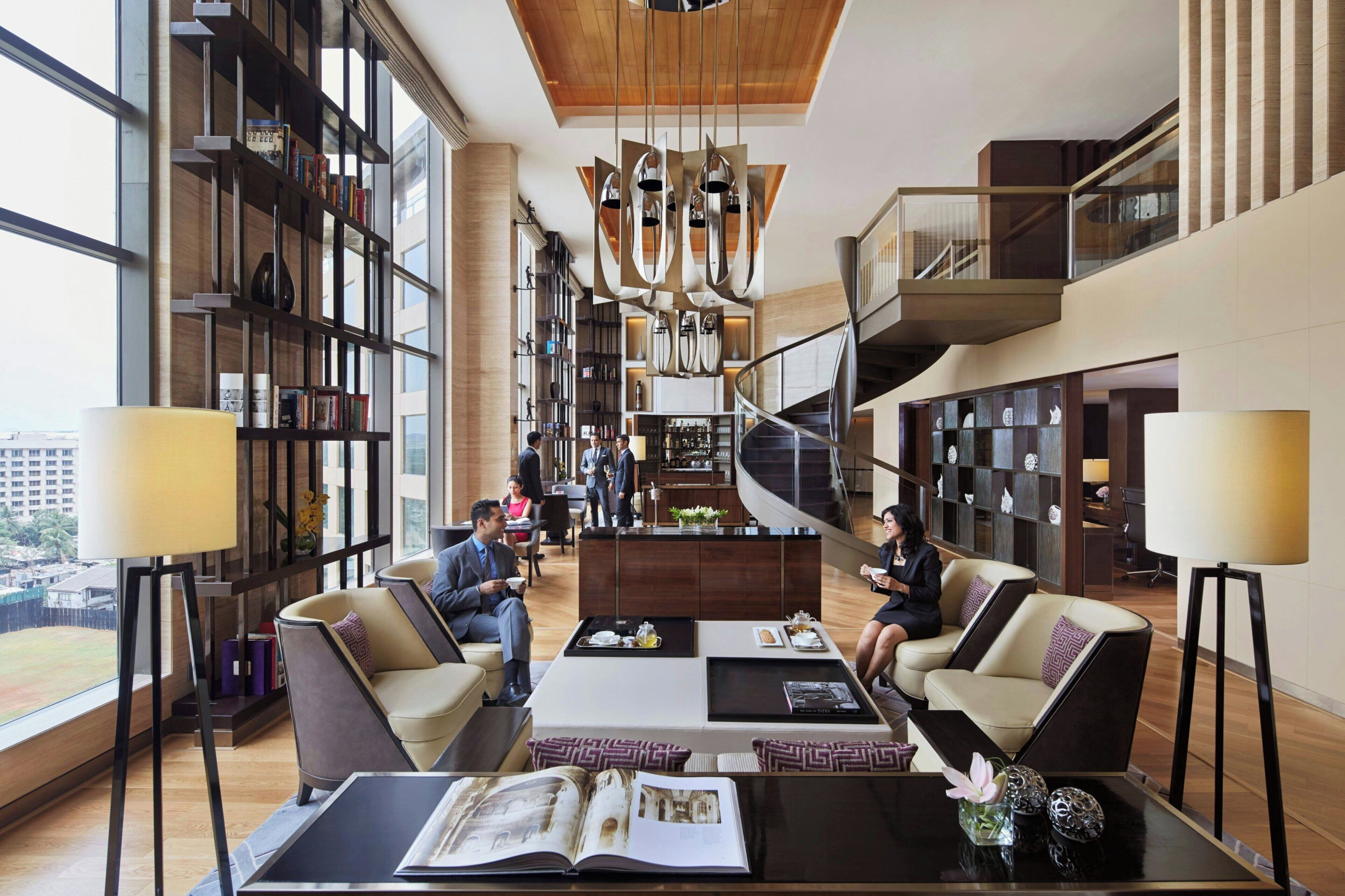 A spacious lobby with a central staircase, seating areas, and a large bookshelf.