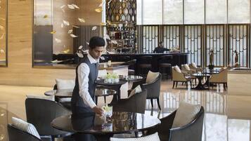 En modern hotellobby med en bardel, sittgrupper och ett stort fönster som släpper in naturligt ljus.