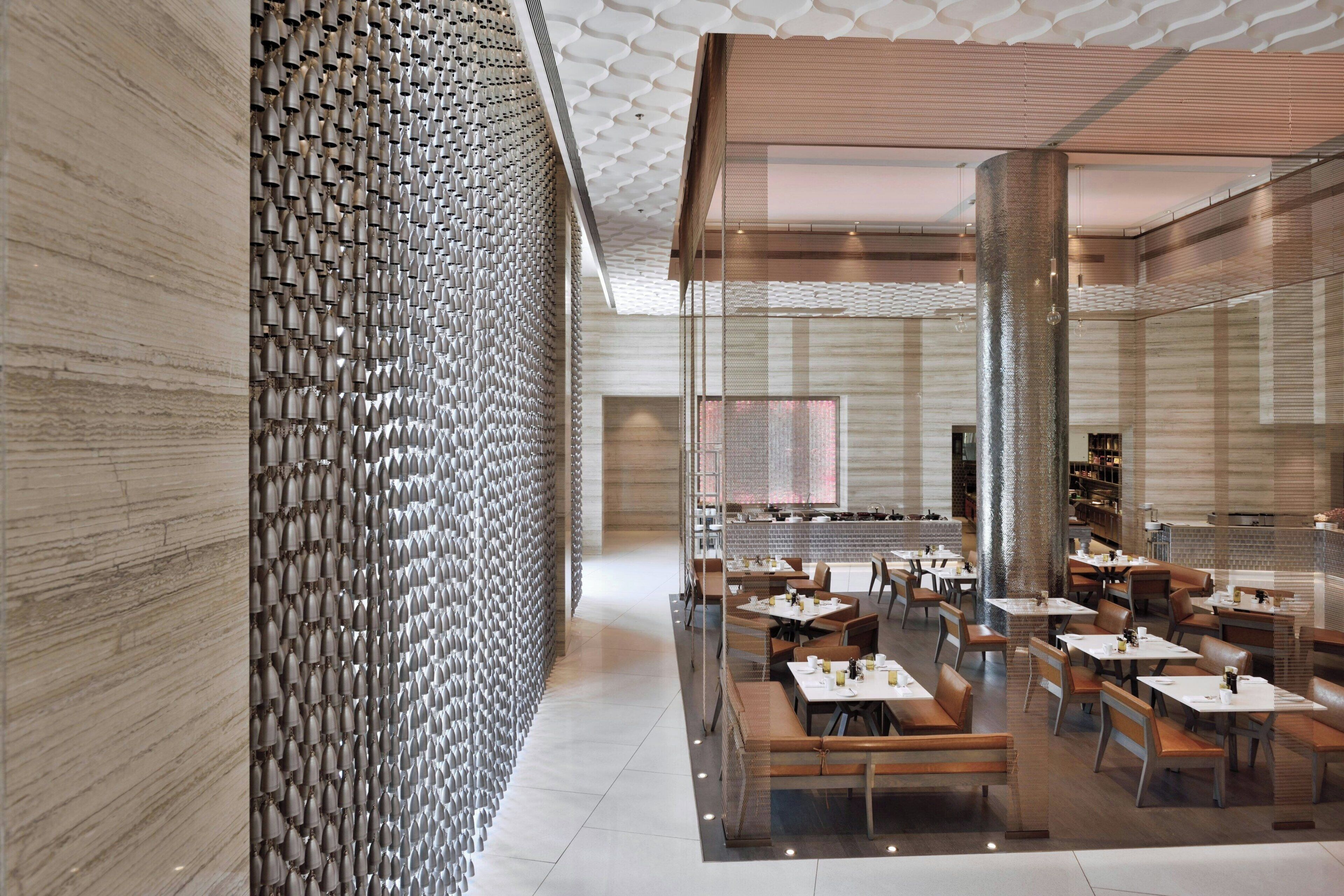 A modern restaurant interior with a patterned wall, wooden ceiling, and a variety of seating arrangements.