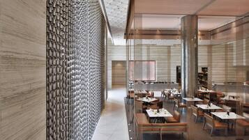A modern restaurant interior with a patterned wall, wooden ceiling, and a variety of seating arrangements.