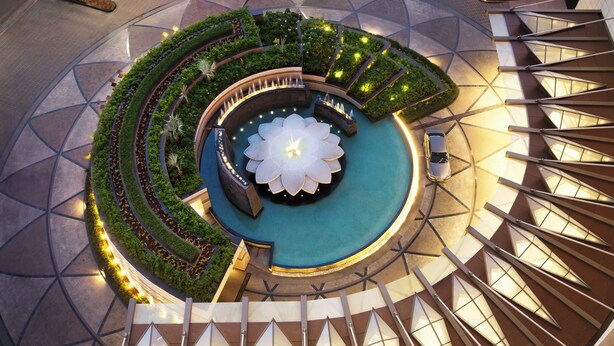 Un atrium circular con una fuente central, rodeado de follaje y una escalera.