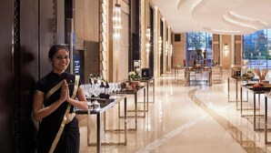Un vestíbulo de hotel con diseño moderno, que presenta un suelo de mármol, una larga recepción y un techo curvo con iluminación integrada.