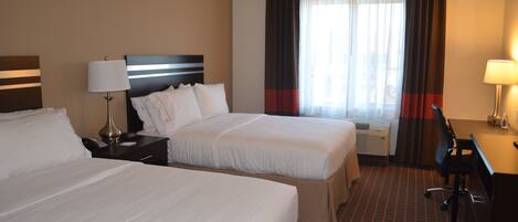 A hotel room with two beds, a desk, a chair, a lamp, and a window with curtains.