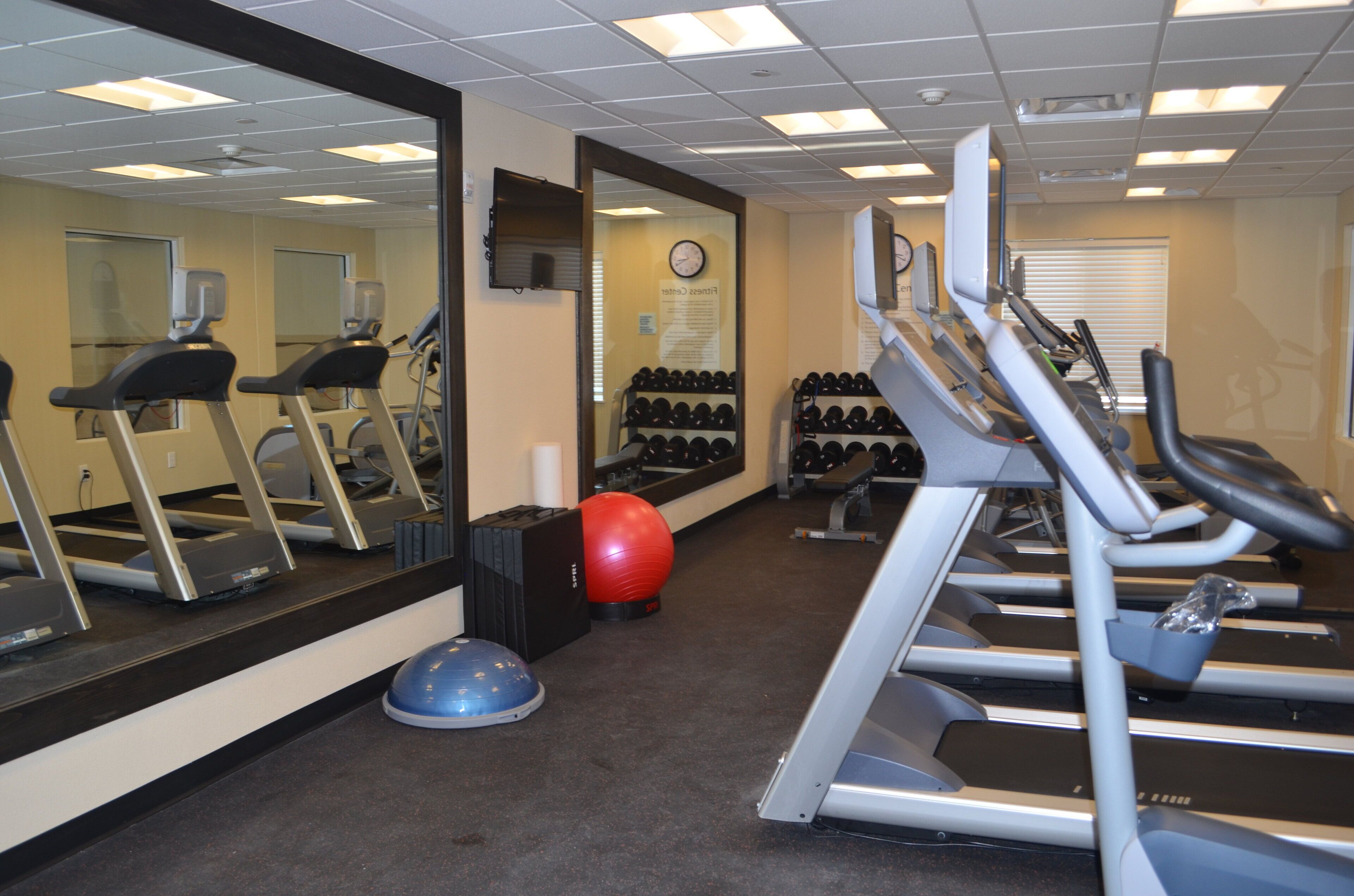 A gym with treadmills, exercise balls, and a mirrored wall.