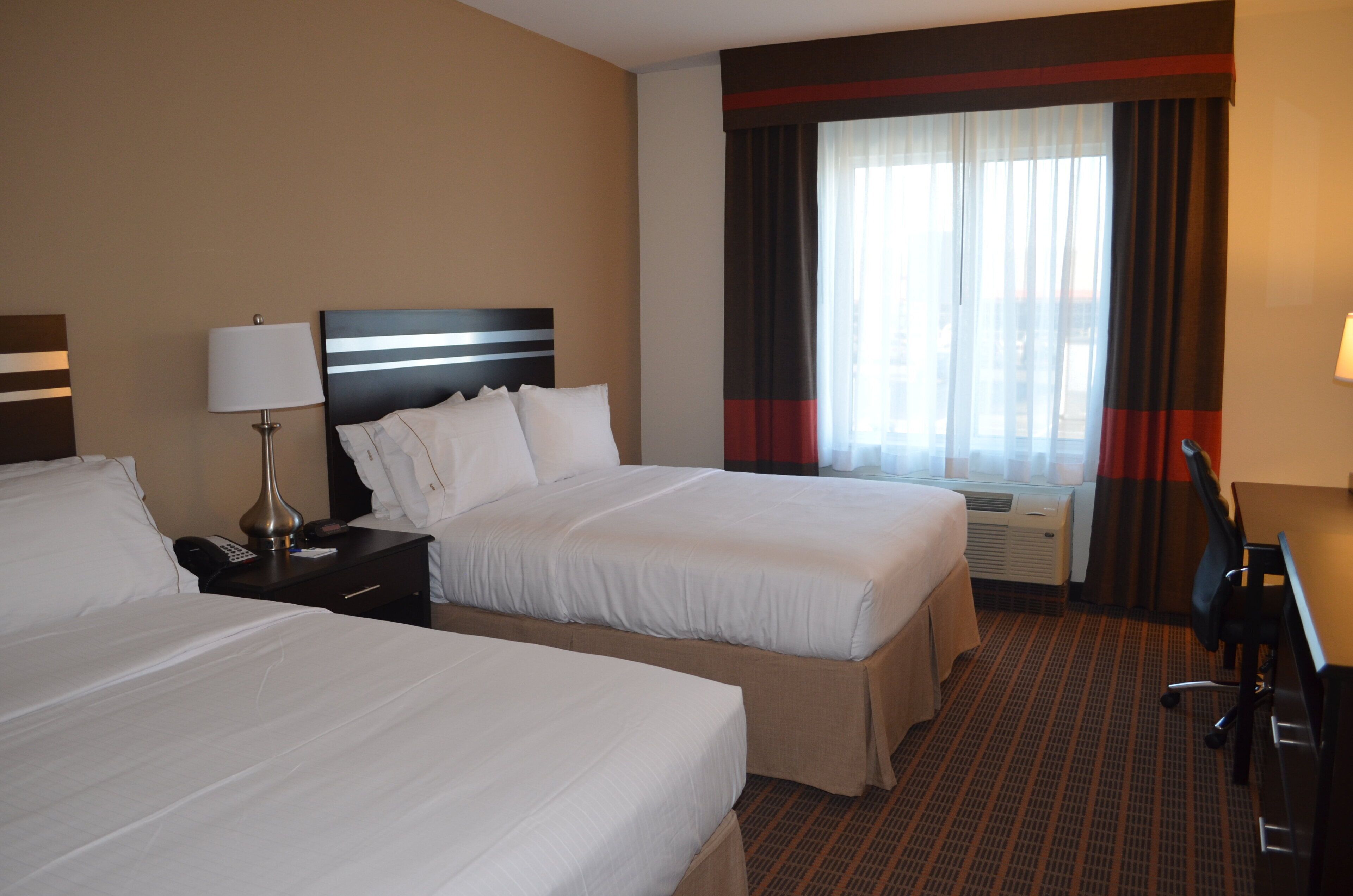 A hotel room with two beds, a desk, a lamp, and a window with curtains.
