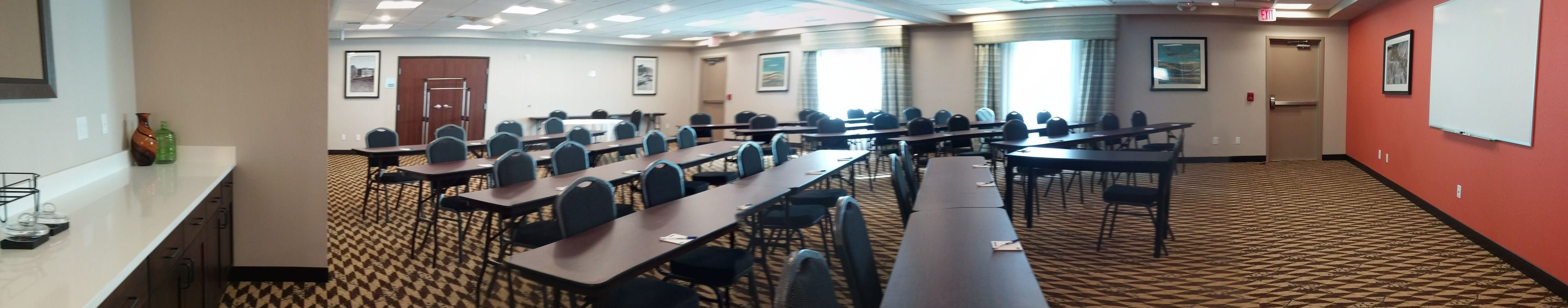 A conference room with multiple tables and chairs, a patterned carpet, and framed pictures on the walls.