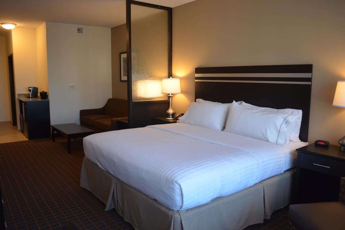 A hotel room with a large bed, a desk, a chair, and a nightstand with a lamp.