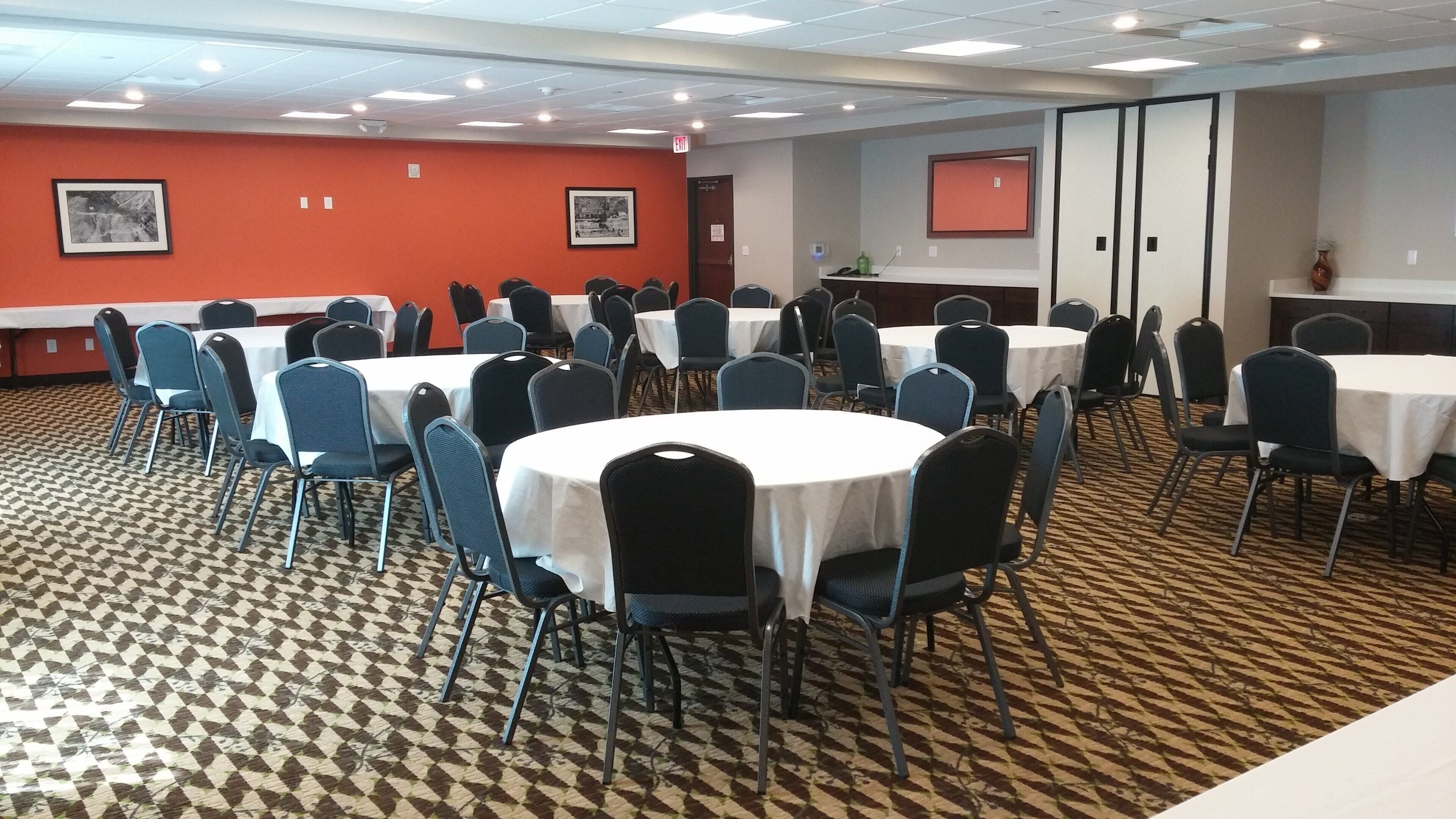 A conference room with round tables and chairs, a patterned carpet, and framed pictures on the walls.
