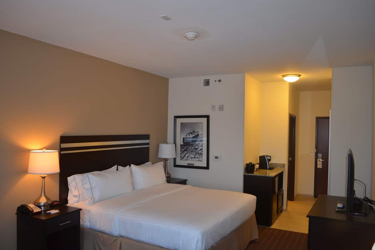 A hotel room with a bed, bedside tables, a desk with a chair, a television, and a framed picture on the wall.