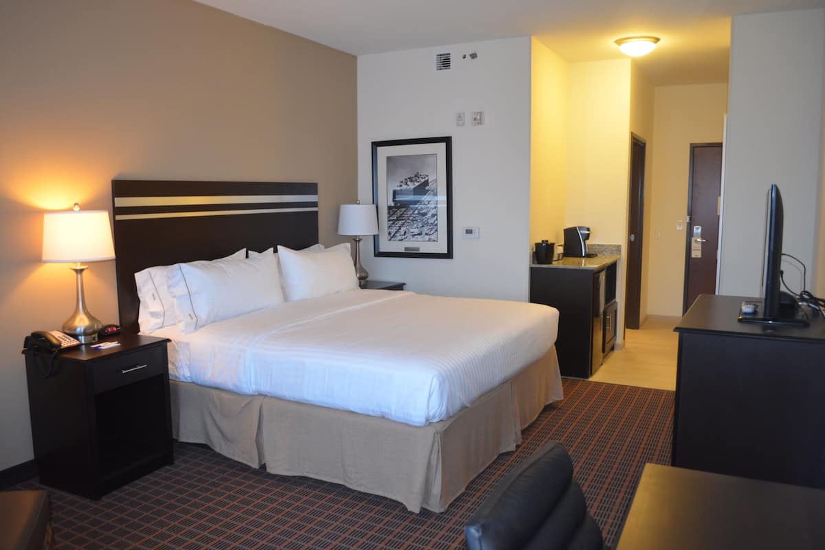 A hotel room with a large bed, bedside tables, a desk with a chair, a TV, and a framed picture on the wall.