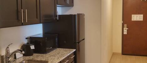 A kitchen with dark cabinets, a stainless steel sink, a black refrigerator, and a granite countertop.