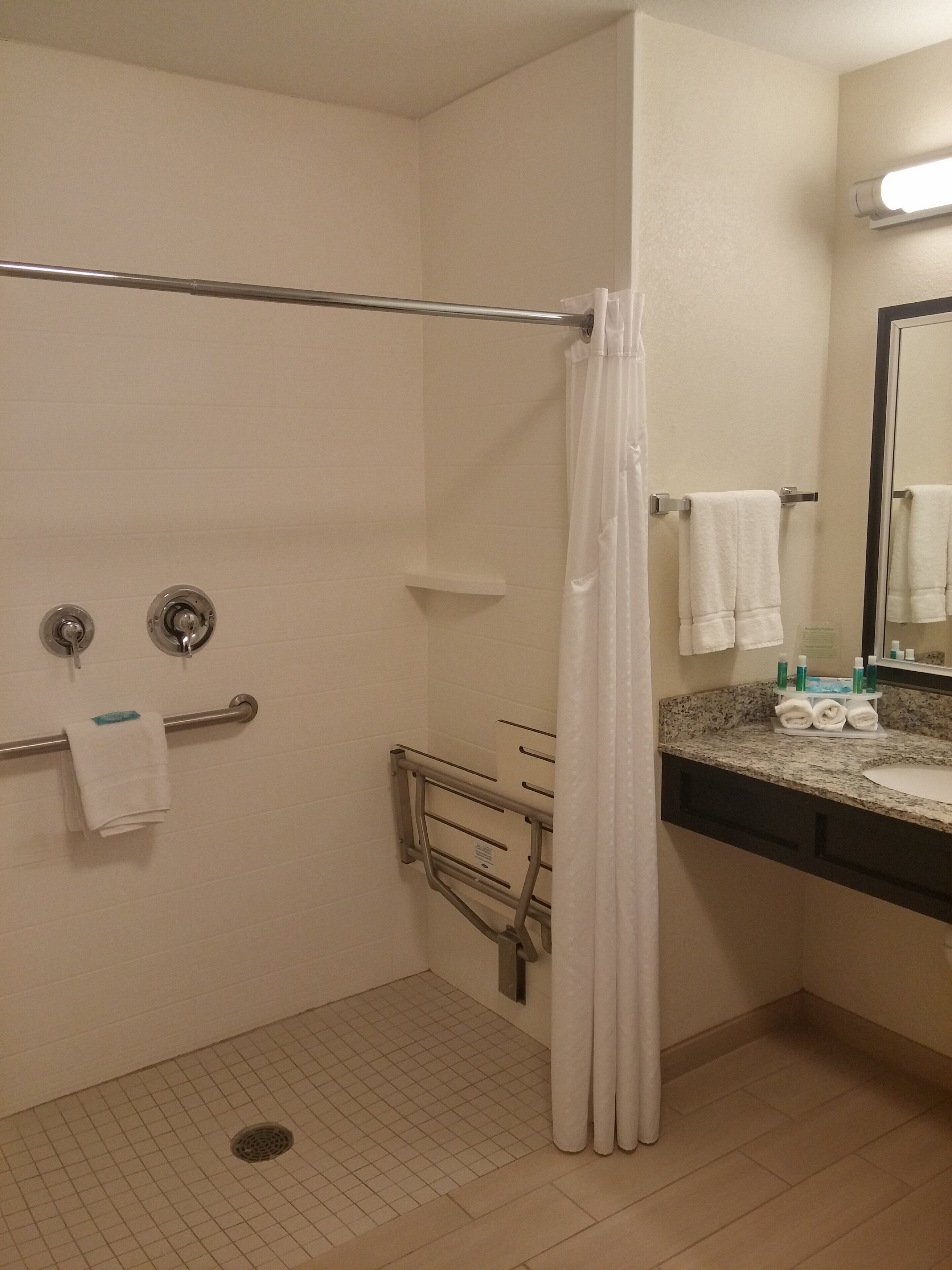 A bathroom with a shower, a grab bar, a towel rack, and a sink with toiletries.