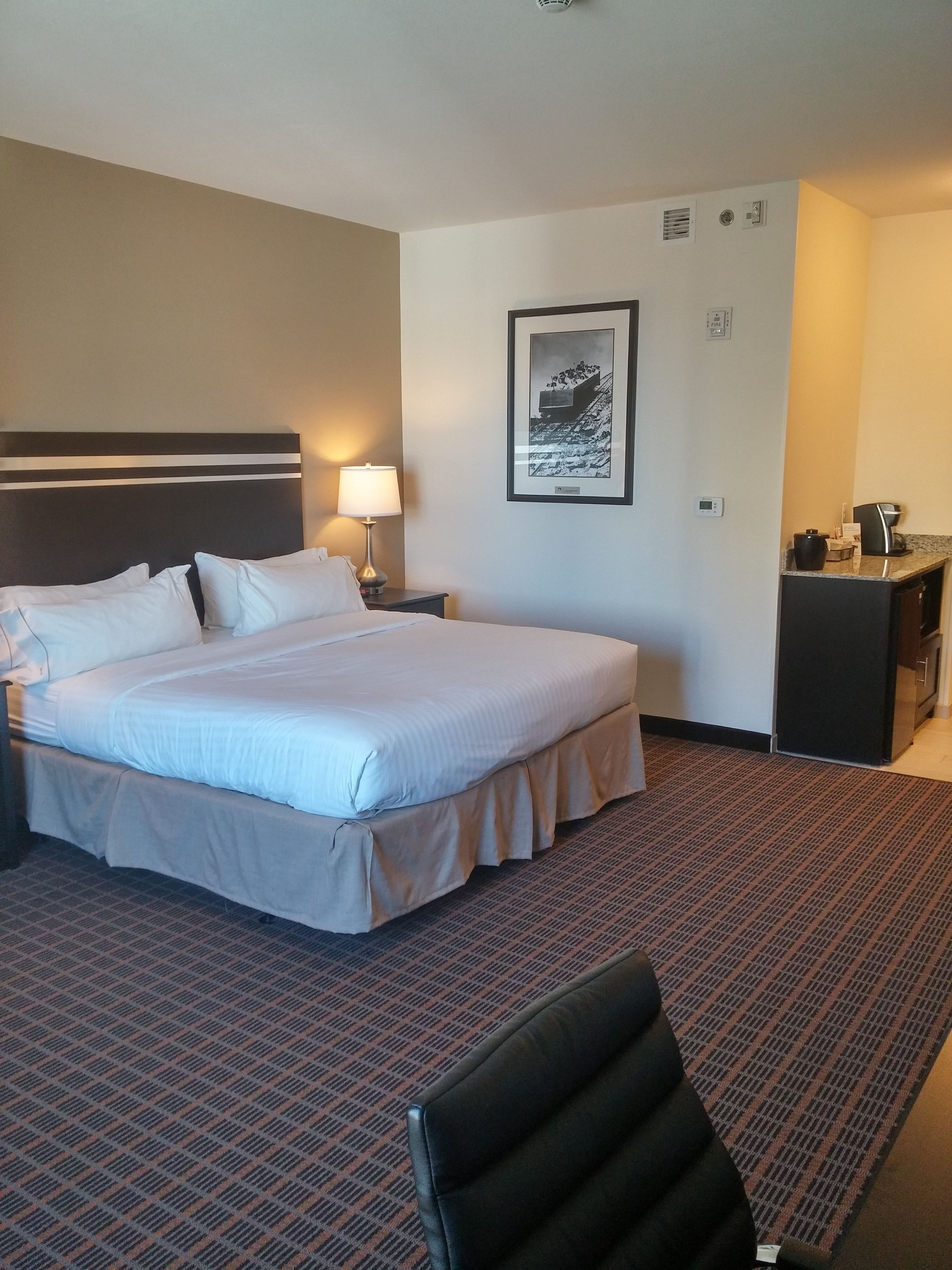 Ein Hotelzimmer mit einem großen Bett, einem Schreibtisch, einem Stuhl und einem gerahmten Bild an der Wand.