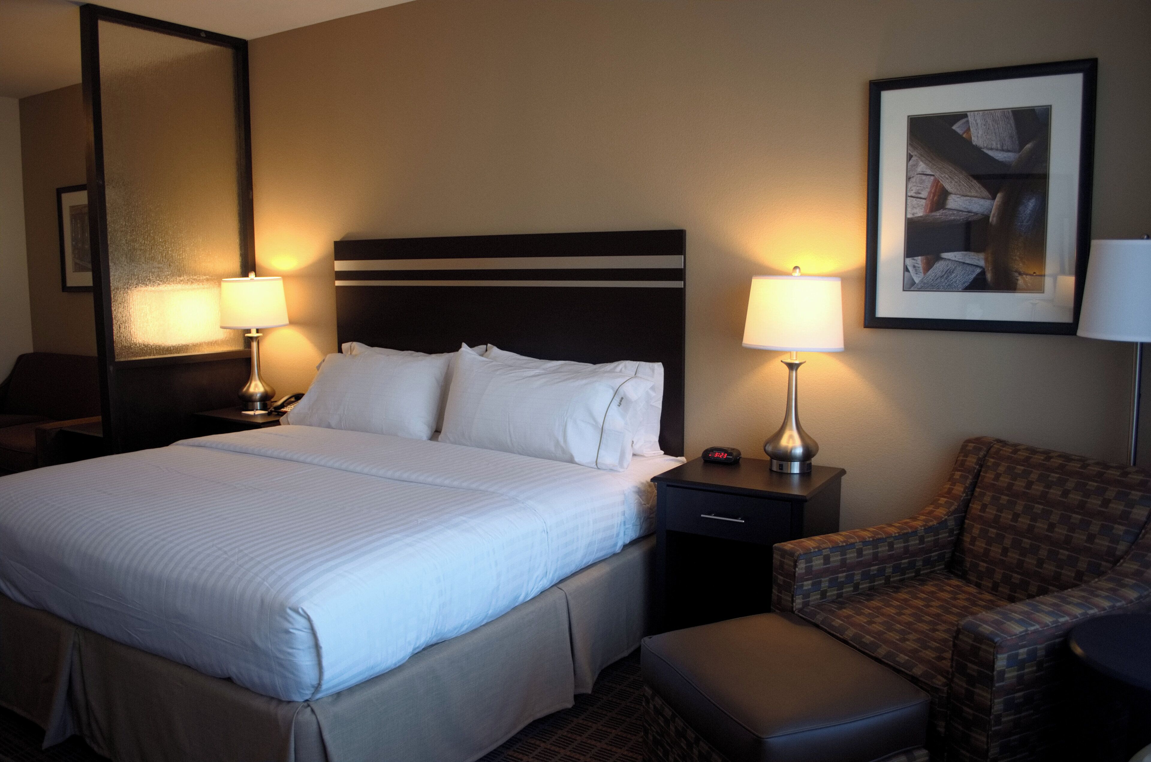 Une chambre d’hôtel avec un grand lit, deux tables de chevet avec des lampes, une chaise et un tableau encadré au mur.