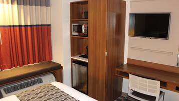 Habitación de hotel compacta con kitchenette, microondas, refrigerador pequeño, televisión de pantalla plana y cama con ropa de cama estampada.
