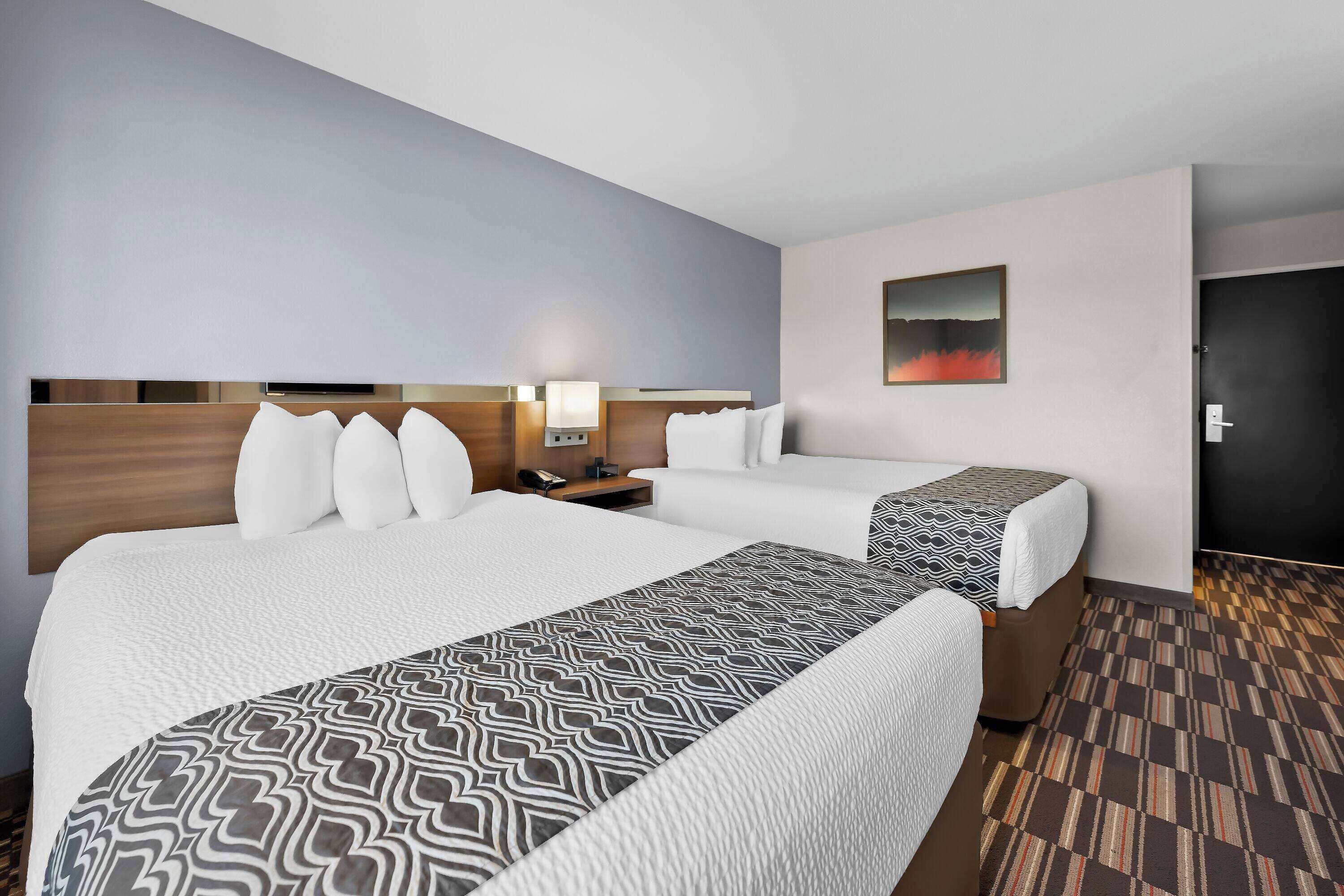 Ein Hotelzimmer mit zwei Betten, einem Nachttisch, einer Lampe, einem Bild an der Wand und einer Tür.