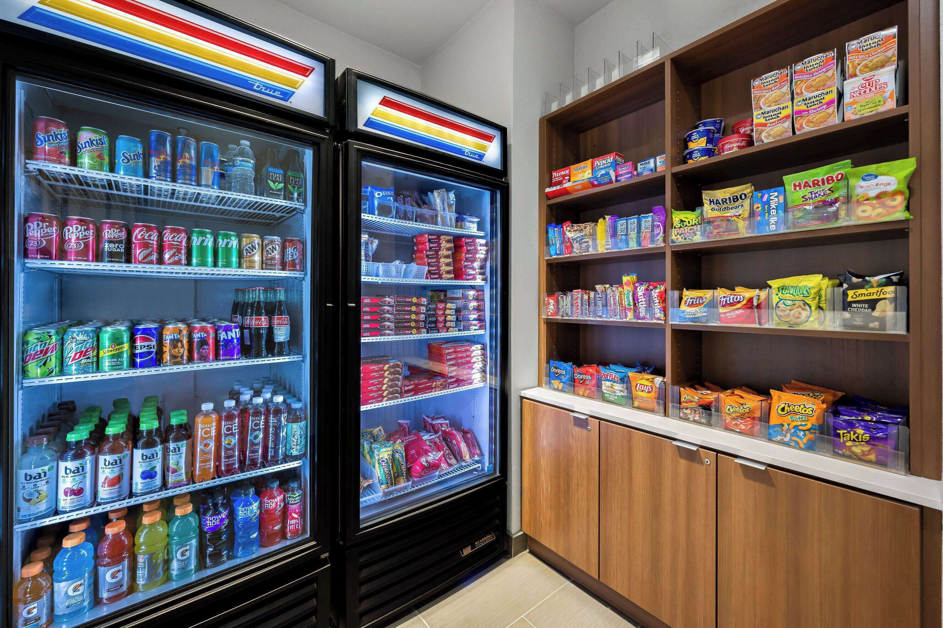 Un distributeur automatique proposant diverses boissons et collations, ainsi que des étagères adjacentes remplies d’aliments emballés.