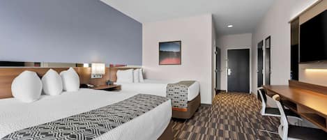 A hotel room with two beds, a desk, a TV, and a patterned carpet.