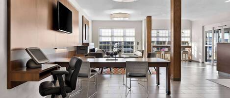 A modern office space with a large desk, chairs, a flat-screen TV, and a large window providing natural light.