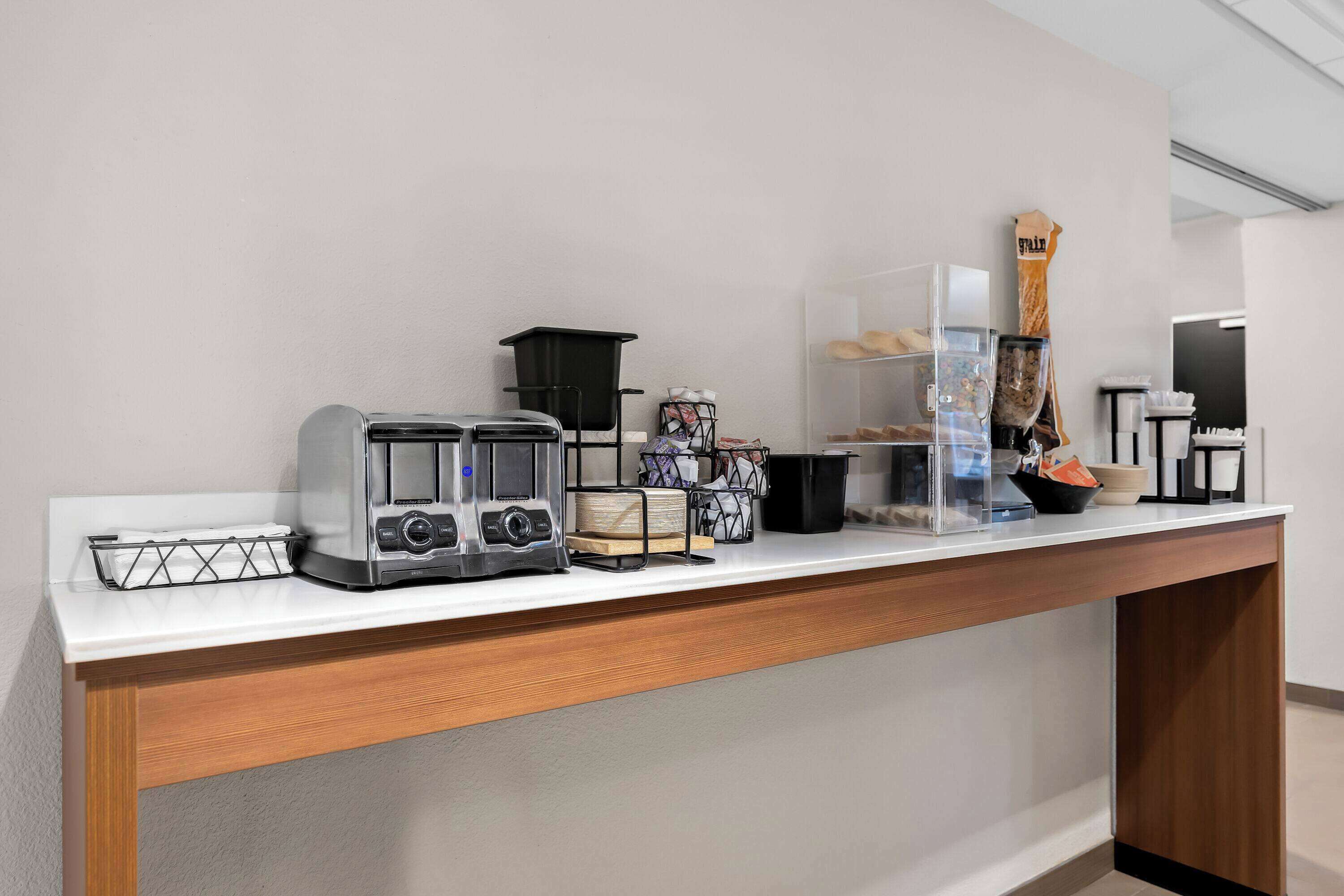 A kitchenette with a coffee maker, toaster, and a clear plastic container on a white countertop.