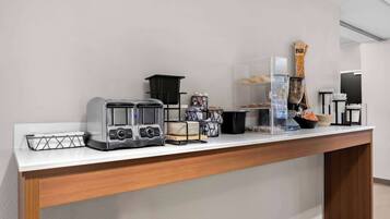 A kitchenette with a coffee maker, toaster, and a clear plastic container on a white countertop.