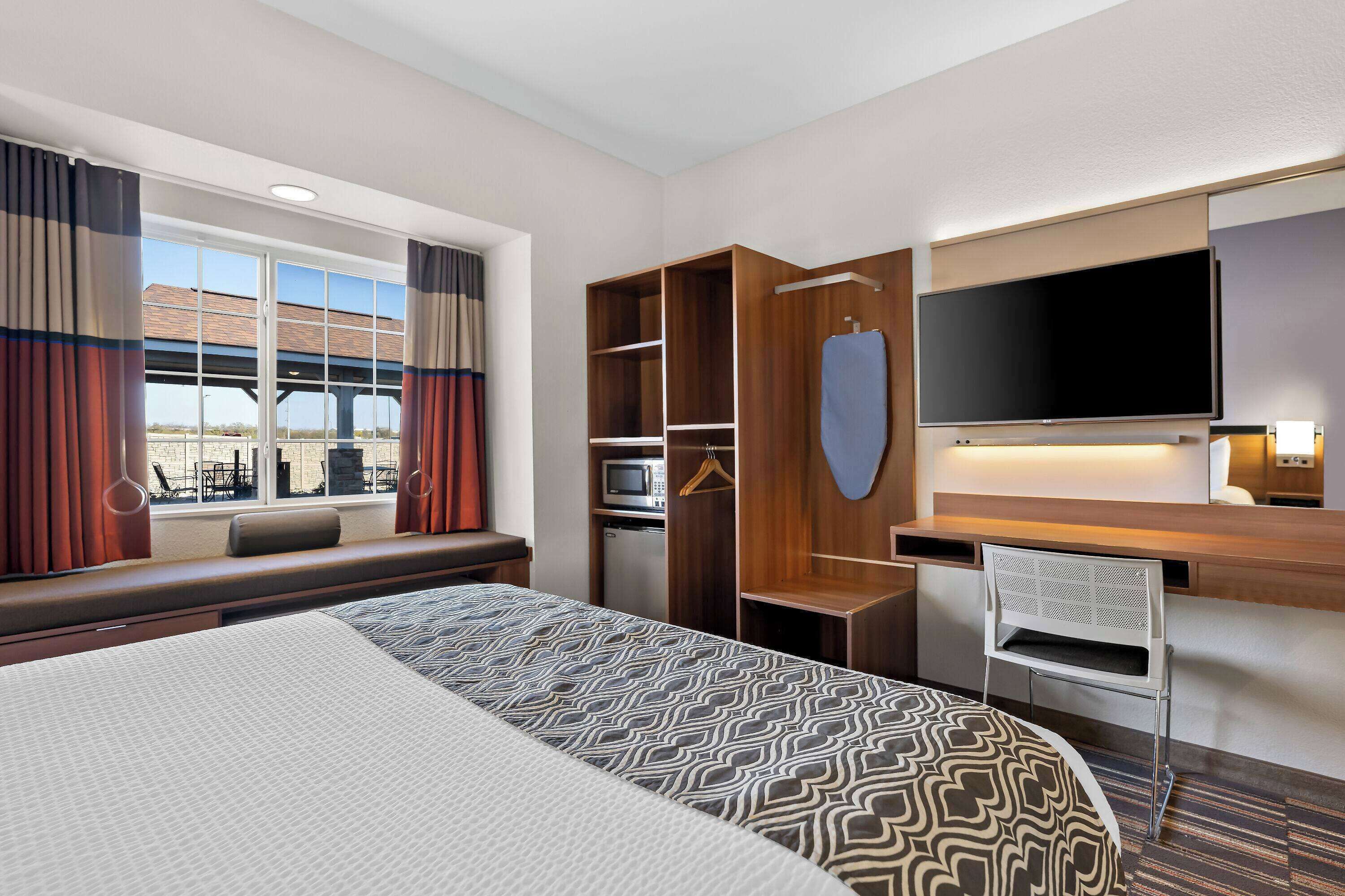 Ein Hotelzimmer mit einem großen Bett, einem Schreibtisch mit Fernseher, einer Mikrowelle und einer Sitzecke am Fenster.