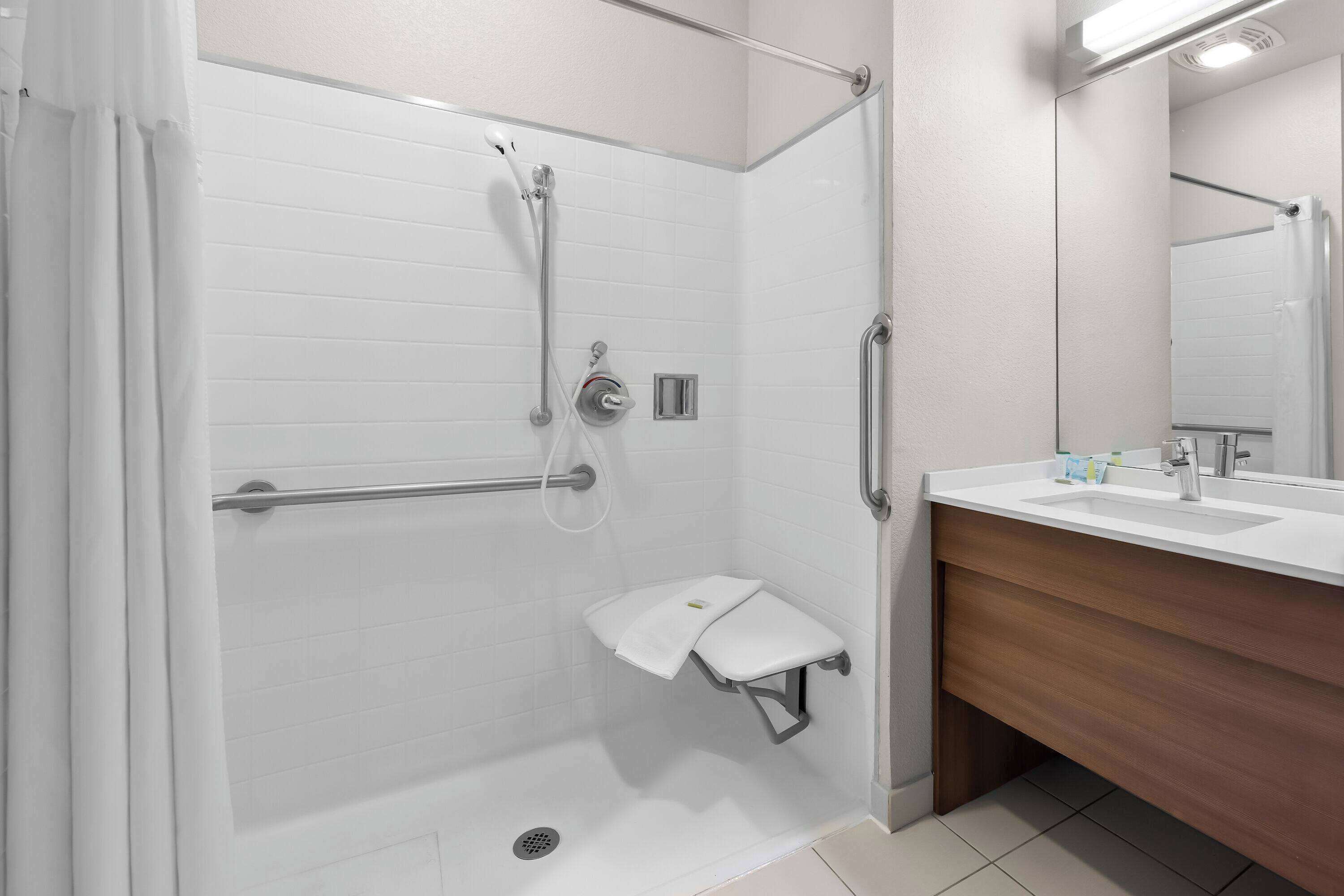 Une salle de bain moderne dotée d’une douche à l’italienne, de barres d’appui, d’un porte-serviettes et d’un meuble-lavabo avec un miroir.