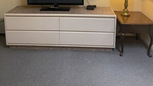 Une chambre d’hôtel avec un téléviseur à écran plat posé sur une commode blanche, une lampe sur une petite table et un sol recouvert de moquette.