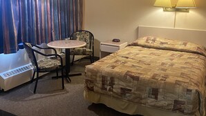 Une chambre d’hôtel comprenant un lit, une chaise, une petite table, un radiateur et deux lampes fixées au mur.
