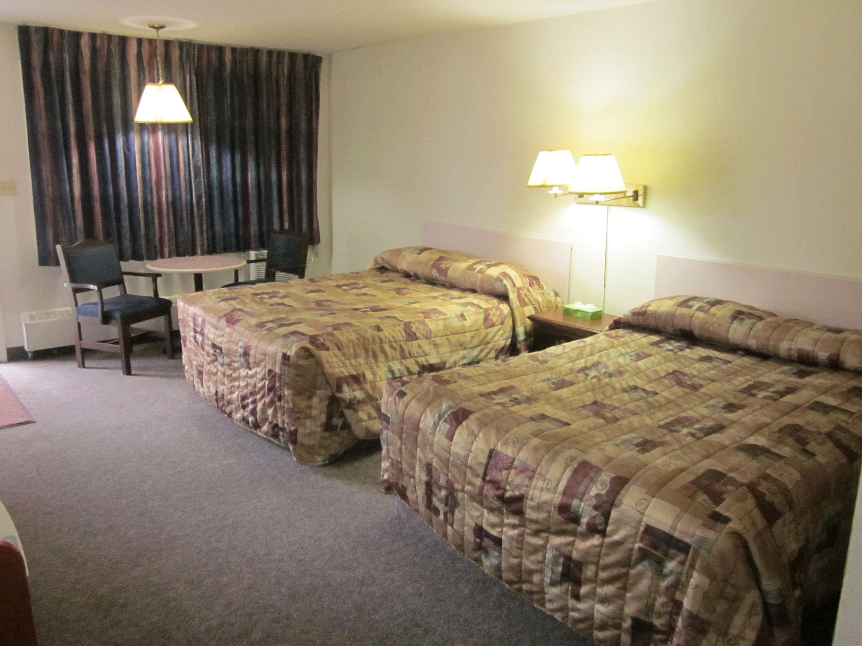 Hotellihuone, jossa on kaksi sänkyä, työpöytä, tuoli ja lamppu.