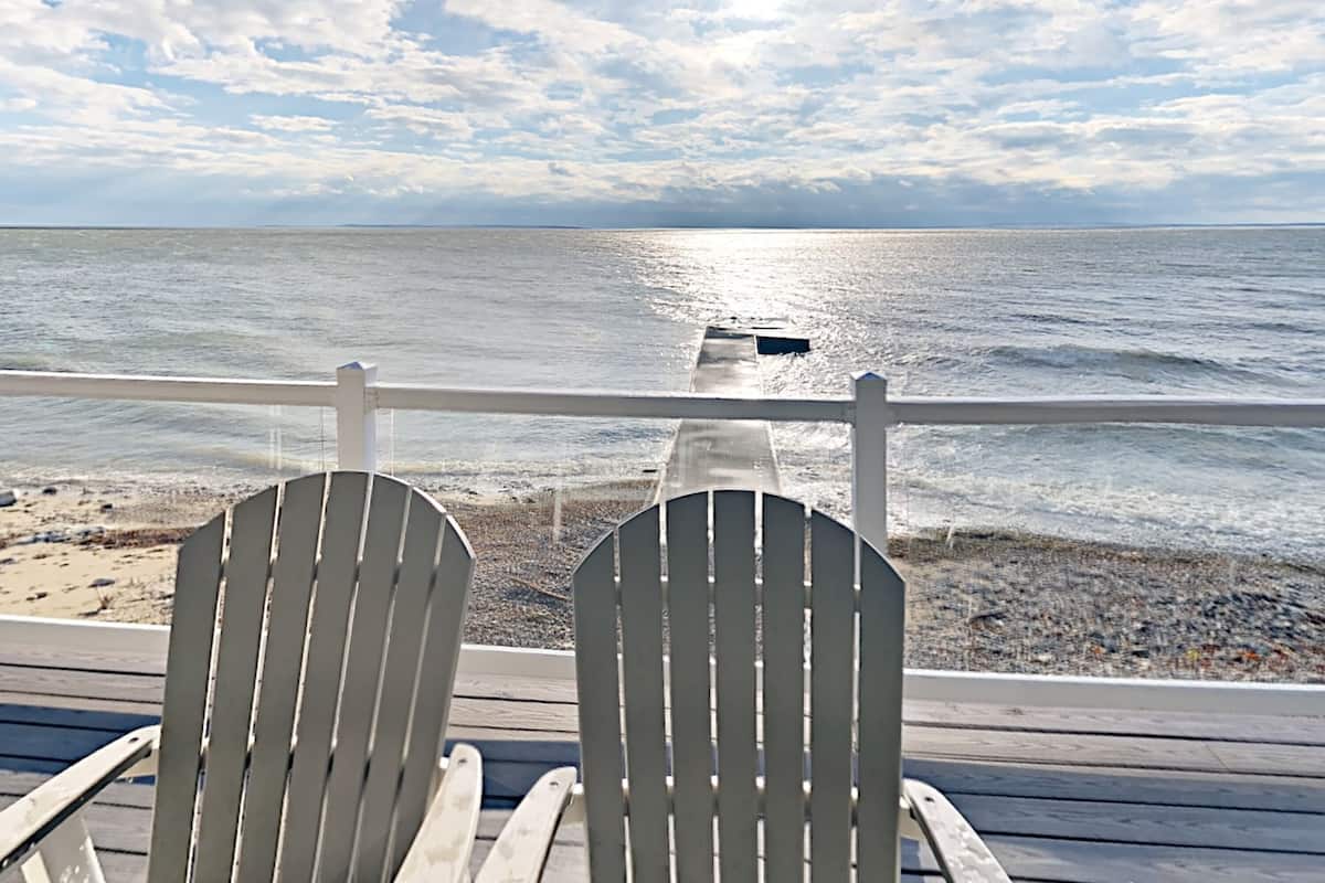 Duas cadeiras Adirondack de frente para uma praia, com um deck de madeira e guarda-corpo.