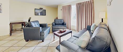 A living room with two sofas, a coffee table, and a flat-screen TV mounted on the wall.