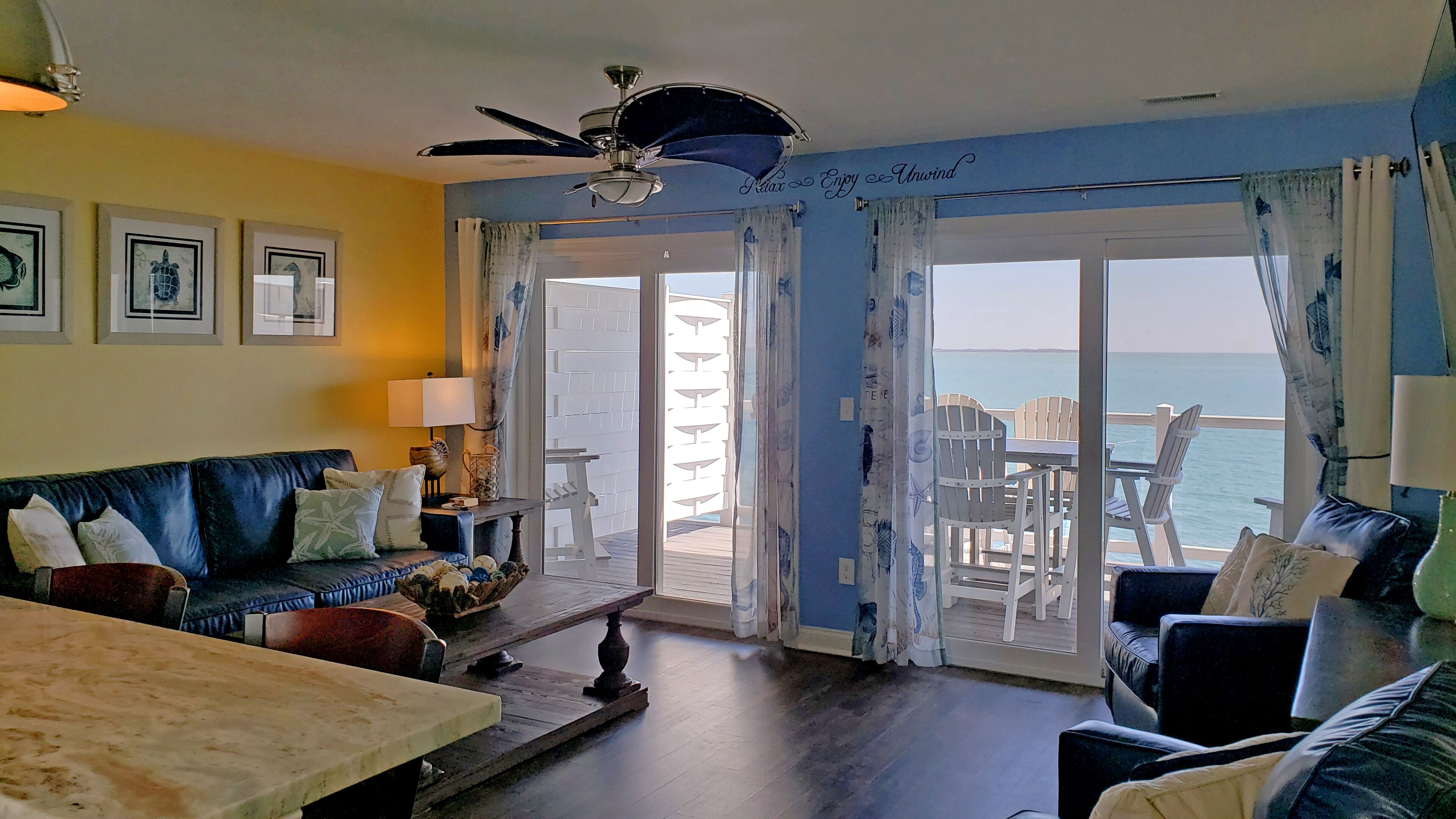 A living room with a sofa, a coffee table, and a view of the sea through a glass door.