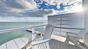 A wooden deck with a railing overlooking a calm body of water and a cloudy sky.
