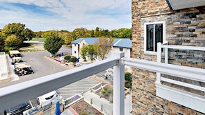 A view from a balcony overlooking a parking lot with golf carts, a building with a stone facade, and a clear sky.