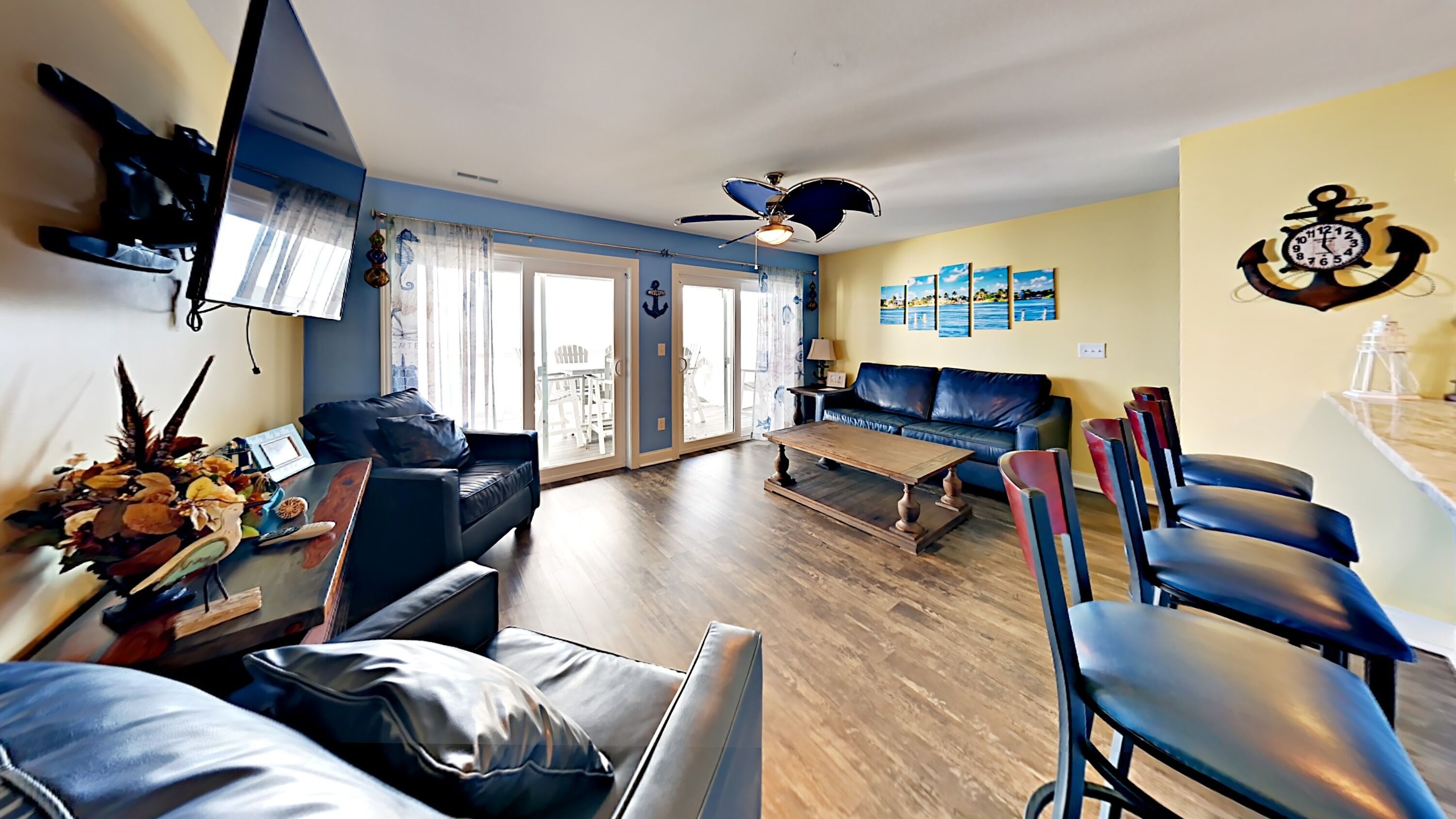 A living room with a sofa, coffee table, and chairs, a ceiling fan, and a wall with nautical-themed decorations.