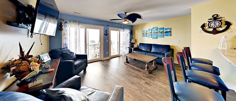 A living room with a sofa, coffee table, and chairs, a ceiling fan, and a wall with nautical-themed decorations.