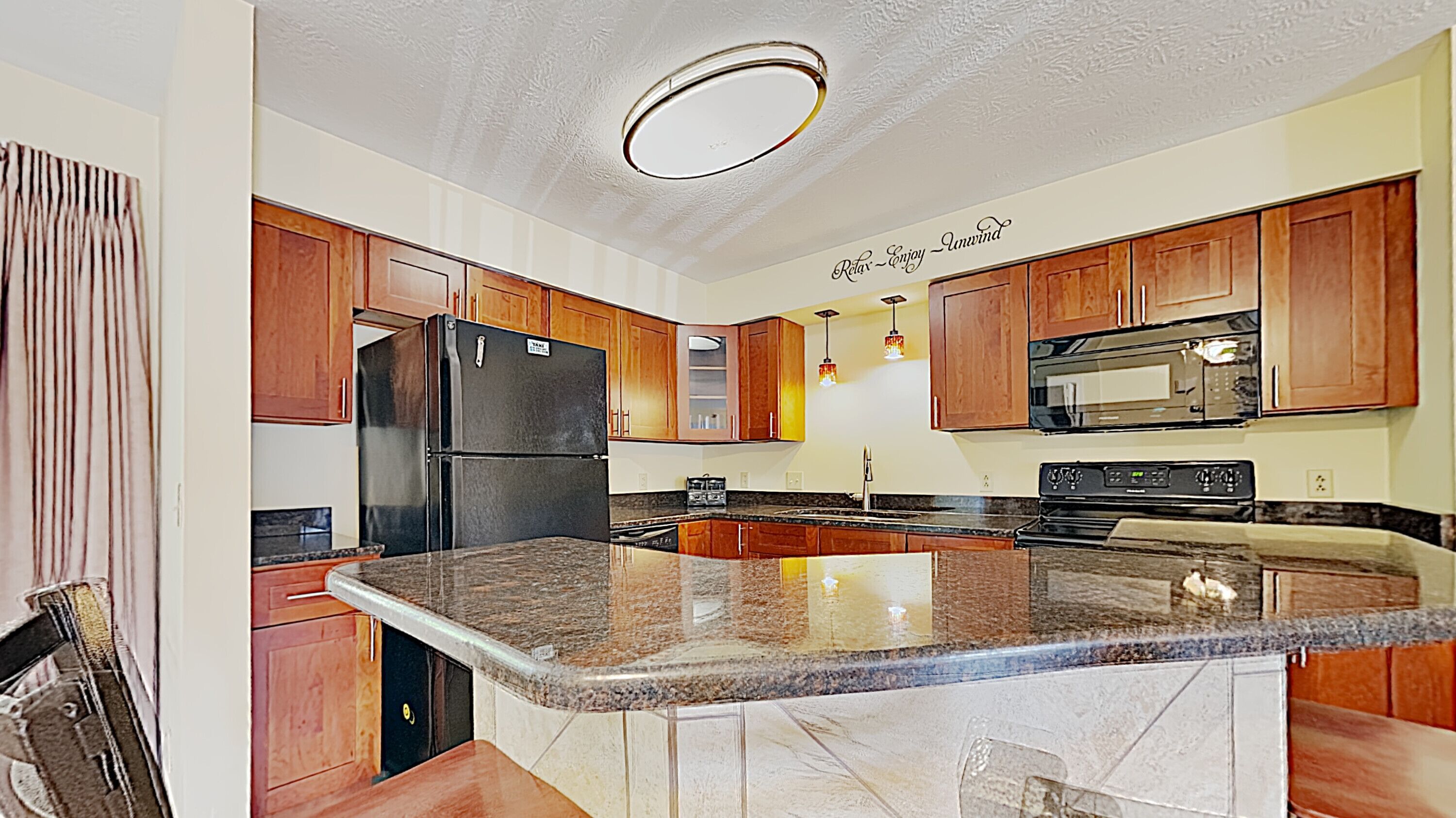 Una cocina moderna con armarios de madera, un refrigerador negro, un microondas y una encimera de granito.