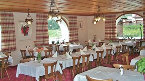 Un restaurante con varias mesas y sillas, vigas de madera en el techo y amplias ventanas con cortinas.