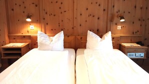 Una habitación con dos camas, paredes de paneles de madera, lámparas de noche y una mesita con un teléfono.