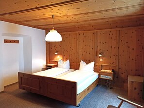 A wooden-paneled room with a bed, bedside lamps, and a small table. - Hotel Acla Filli (Zernez)