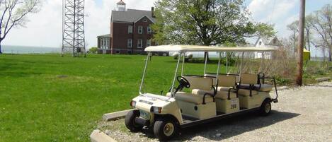 Un véhicule de golf est garé sur un chemin de gravier, avec un champ herbeux et un bâtiment en briques en arrière-plan.