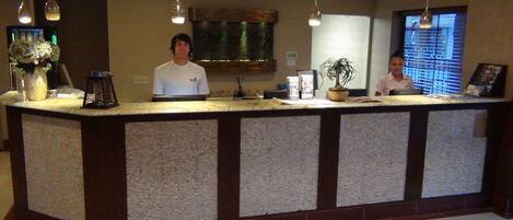 A reception desk with a marble counter, hanging pendant lights, a potted plant, and a framed picture.