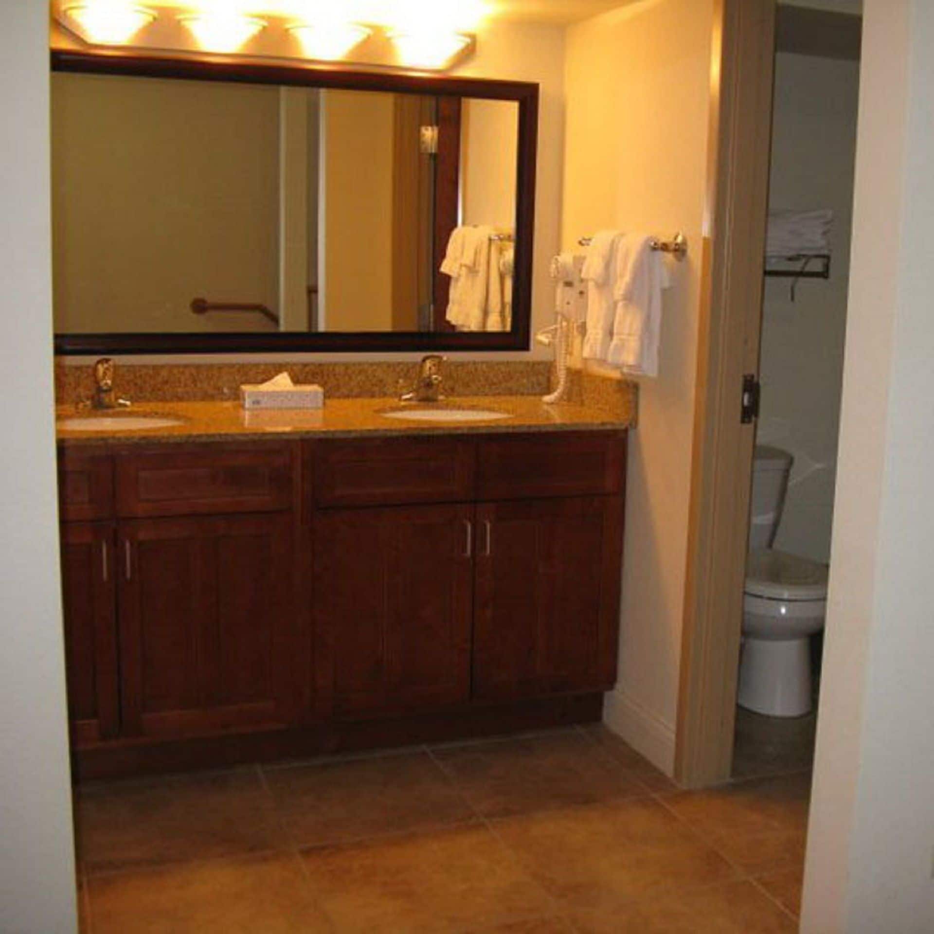 A bathroom with a wooden vanity, a mirror, and a toilet.